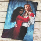 A printed pouch featuring an illustration of a dark-skinned woman in a red dress embracing a pale elf with long red hair, dressed in white, standing together in a blue, misty forest.