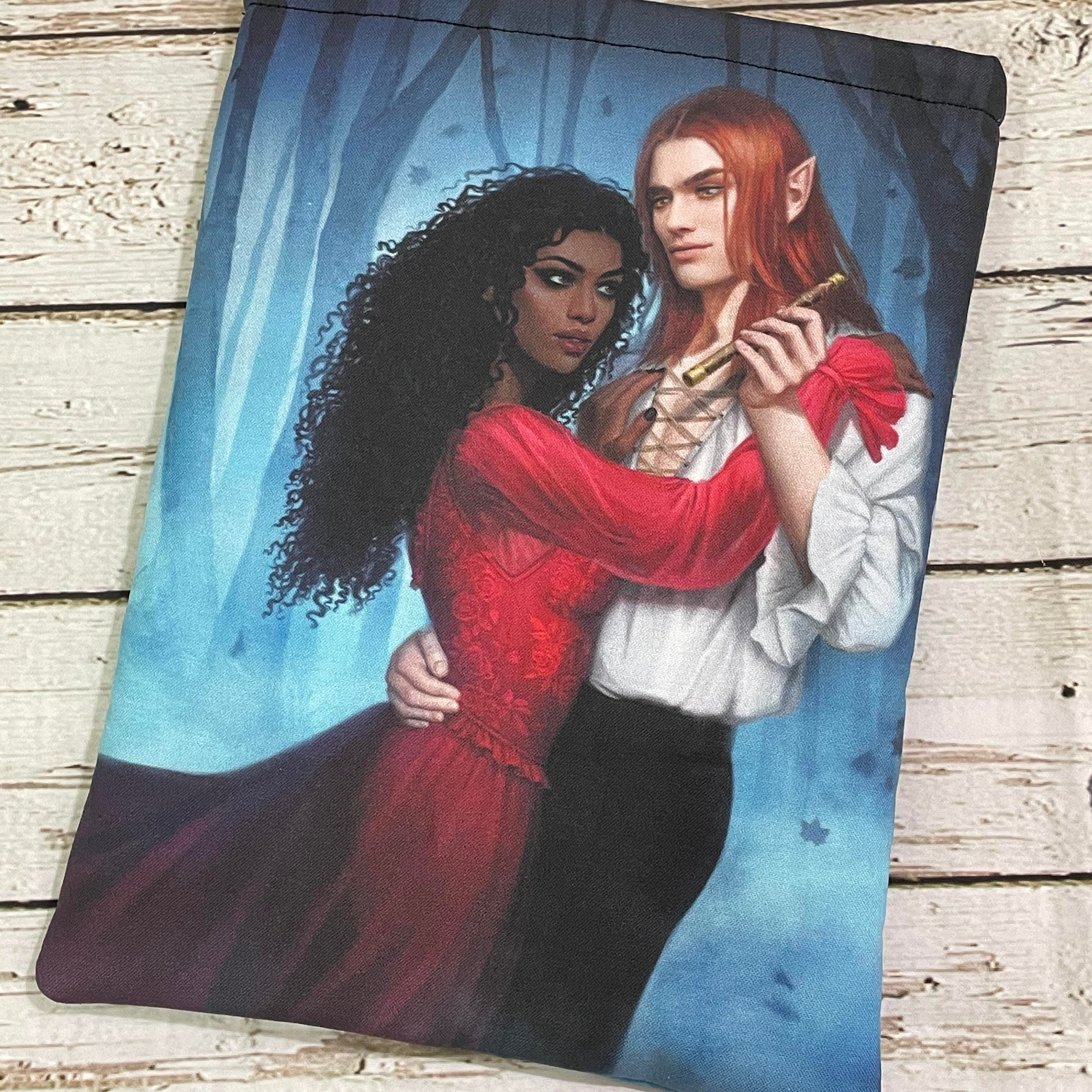 A printed pouch featuring an illustration of a dark-skinned woman in a red dress embracing a pale elf with long red hair, dressed in white, standing together in a blue, misty forest.