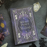 Book titled 'Wicked Prince of Mirrors' on a dark surface with decorative elements.